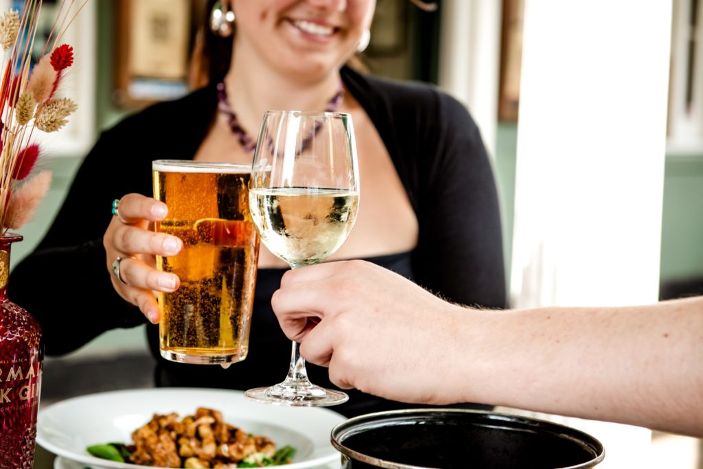 A couple clinking a pint of beer and a glass of wine in celebration while dining outside on the Pantiles