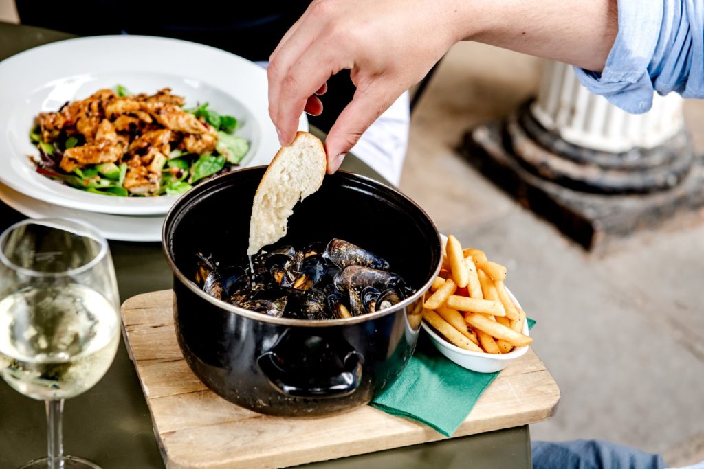 A person's dipping French bread into a pot of Moules Mariniere while enjoying lunch at the Ragged Trousers Brasserie on the Pantiles in Tunbridge Wells
