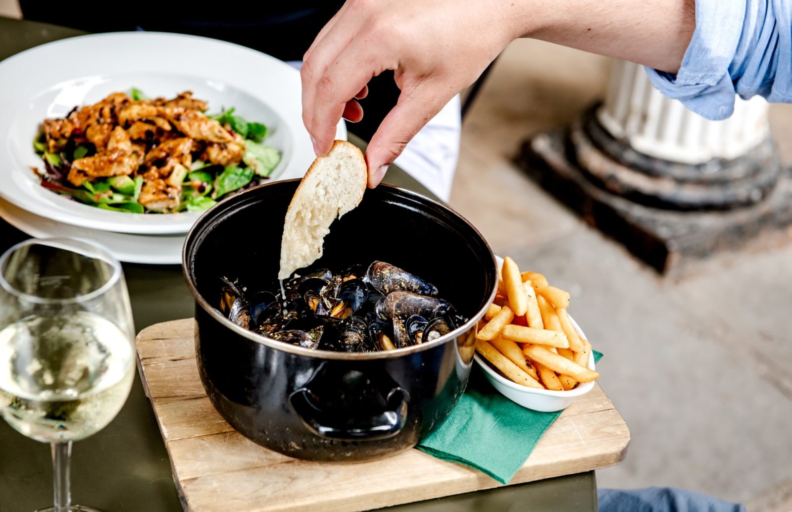 A person's dipping French bread into a pot of Moules Mariniere while enjoying lunch at the Ragged Trousers Brasserie on the Pantiles in Tunbridge Wells