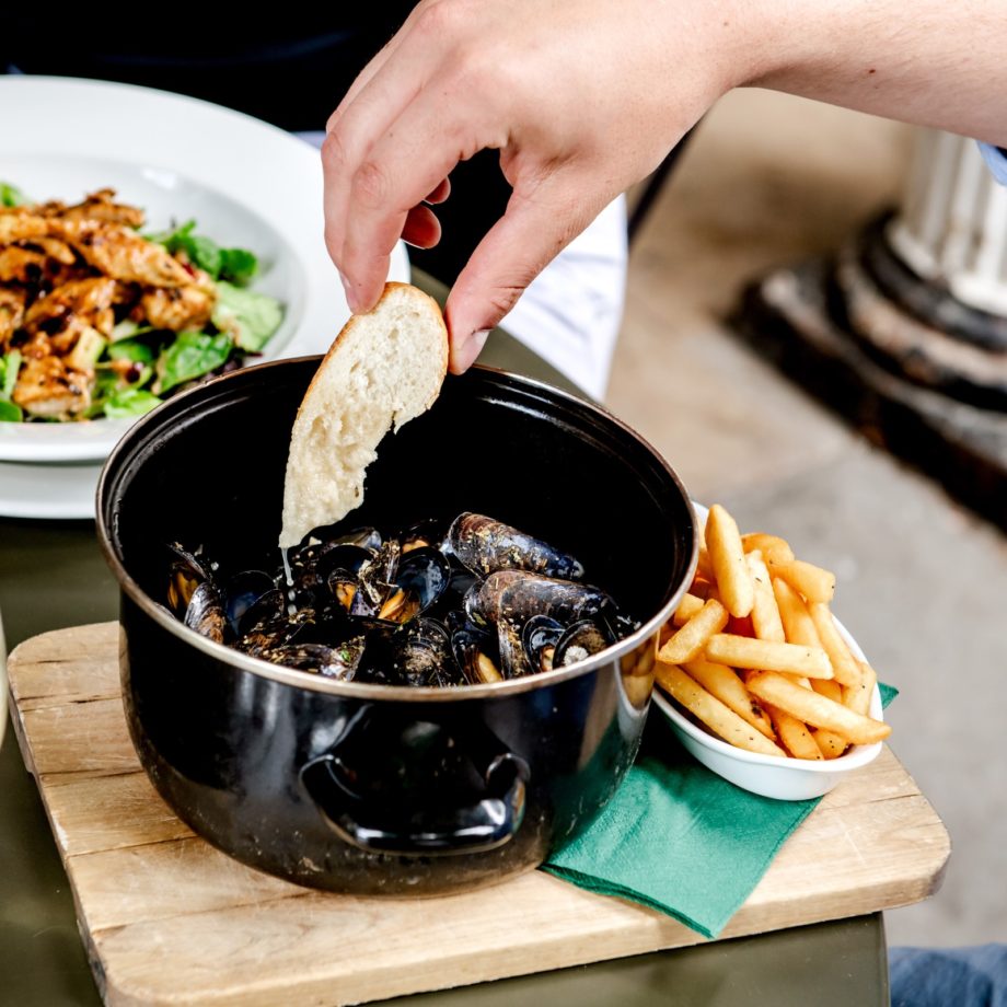 A person's dipping French bread into a pot of Moules Mariniere while enjoying lunch at the Ragged Trousers Brasserie on the Pantiles in Tunbridge Wells