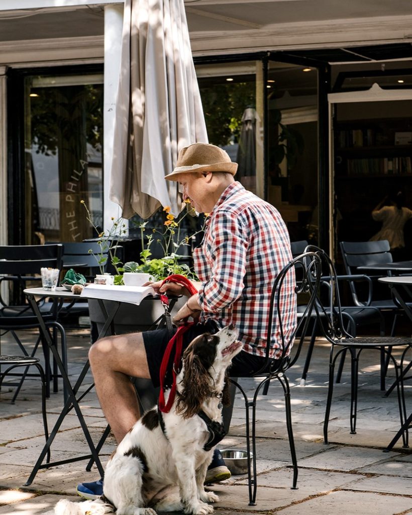 Man sitting outside the Philanthropist cafe on the Pantiles in Tunbridge Wells, with coffee, book, and his dog.